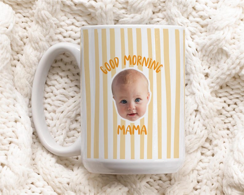 May include: A white ceramic mug featuring a vertical yellow striped pattern. The center of the mug displays a photographic portrait of a baby's face, with the orange text GOOD MORNING arched above the face and the word MAMA printed below it.