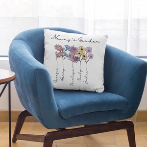 May include: White cushion with the text "Nanny's Garden" and a floral design with five flowers. The names "Georgia", "Harry", "Penelope", "Emily", and "Joshua" are written vertically below the flowers.