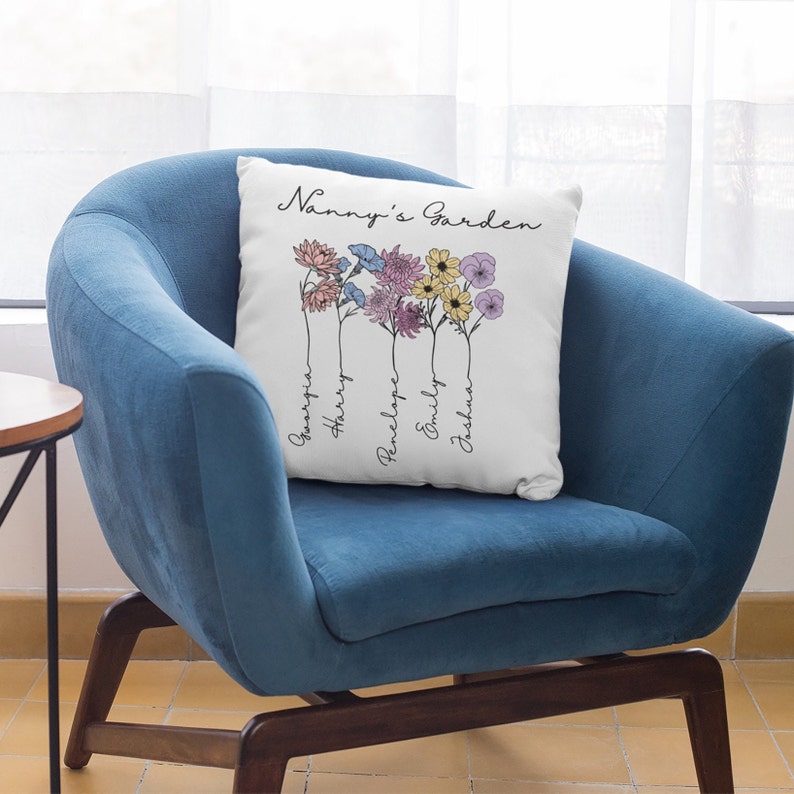 May include: White cushion with the text "Nanny's Garden" and a floral design with five flowers. The names "Georgia", "Harry", "Penelope", "Emily", and "Joshua" are written vertically below the flowers.
