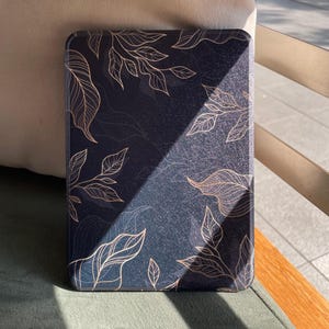 Op de afbeelding: Een donkerblauwe tablethoes met een gouden bladerenpatroon. De rechthoekige hoes heeft een glad oppervlak. Het gouden bladerenpatroon bedekt het gehele oppervlak, wat een decoratieve en elegante uitstraling creëert.