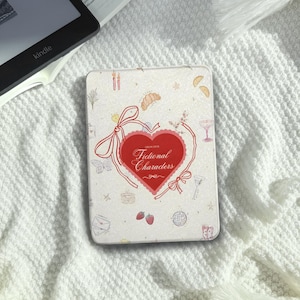 Könnte beinhalten: Eine rechteckige, cremefarbene Hülle mit einem roten Herzdesign und dem Schriftzug "Fictional Characters". Die Hülle ist mit kleinen Illustrationen von Lebensmitteln, Getränken und anderen Objekten verziert. Sie liegt auf einer weißen, strukturierten Oberfläche.