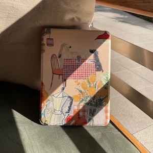 Könnte beinhalten: Rechteckiges dekoratives Tablett mit einer skurrilen Illustration mit zwei Hunden an einem Tisch mit einer rot-weiß karierten Tischdecke. Das Tablett zeigt auch eine Kaffeekanne, Blumen und eine rote Lampe.