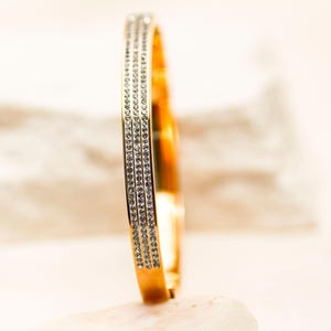 May include: A gold bangle bracelet with a row of clear cubic zirconia stones on each side.