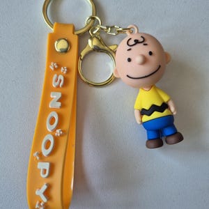 Charming Snoopy Keychain – Charlie Brown Figure with ornage Hand Strap and Snoopy logo