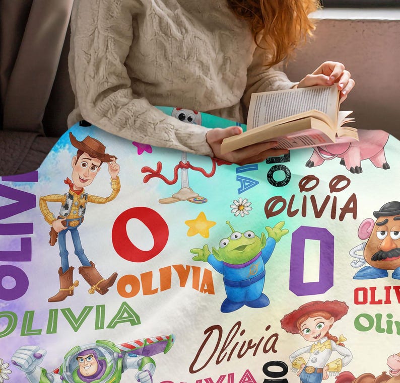 May include: A soft blanket featuring a colorful Toy Story character print with Woody, Buzz Lightyear, Jessie, Mr. Potato Head, and an alien. The design includes the name Olivia in various fonts and colors, alongside stars, flowers, and letters.