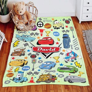 May include: A light green fleece blanket featuring a colorful pattern of various cartoon cars, traffic lights, checkered flags, and trophies. The center displays a red emblem with the name David in white text, surrounded by scattered stars.
