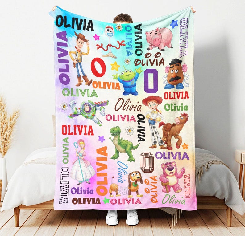 May include: A soft fleece blanket featuring a colorful watercolor background with various cartoon characters including a cowboy, space ranger, cowgirl, dinosaur, and pig. The name OLIVIA is printed repeatedly in various fonts, colors, and sizes.