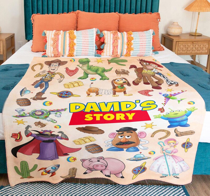May include: A beige fleece blanket featuring a colorful print of Toy Story characters including Woody, Buzz Lightyear, Rex, Slinky Dog, Mr. Potato Head, and Bo Peep. The center displays the text DAVID'S STORY in bold yellow and red lettering.