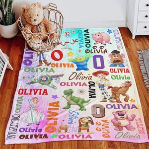 May include: A soft fleece blanket featuring a colorful print of various Toy Story characters including Buzz Lightyear, Woody, Jessie, Rex, and Hamm, interspersed with the name Olivia in multiple fonts and colors, plus small stars and flowers.