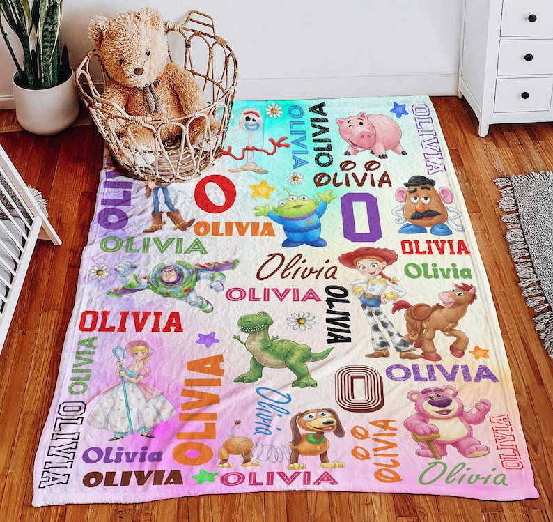 May include: A soft fleece blanket featuring a colorful print of various Toy Story characters including Buzz Lightyear, Woody, Jessie, Rex, and Hamm, interspersed with the name Olivia in multiple fonts and colors, plus small stars and flowers.