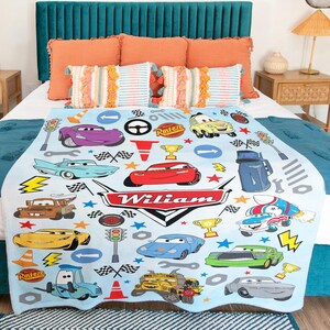 May include: A light blue fleece blanket featuring a repeating pattern of various cartoon race cars, traffic lights, checkered flags, and trophies. The center displays a large red and white emblem with the name Wiliam printed in white text.