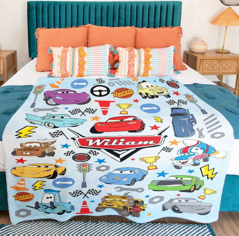 May include: A light blue fleece blanket featuring a repeating pattern of various cartoon race cars, traffic lights, checkered flags, and trophies. The center displays a large red and white emblem with the name Wiliam printed in white text.