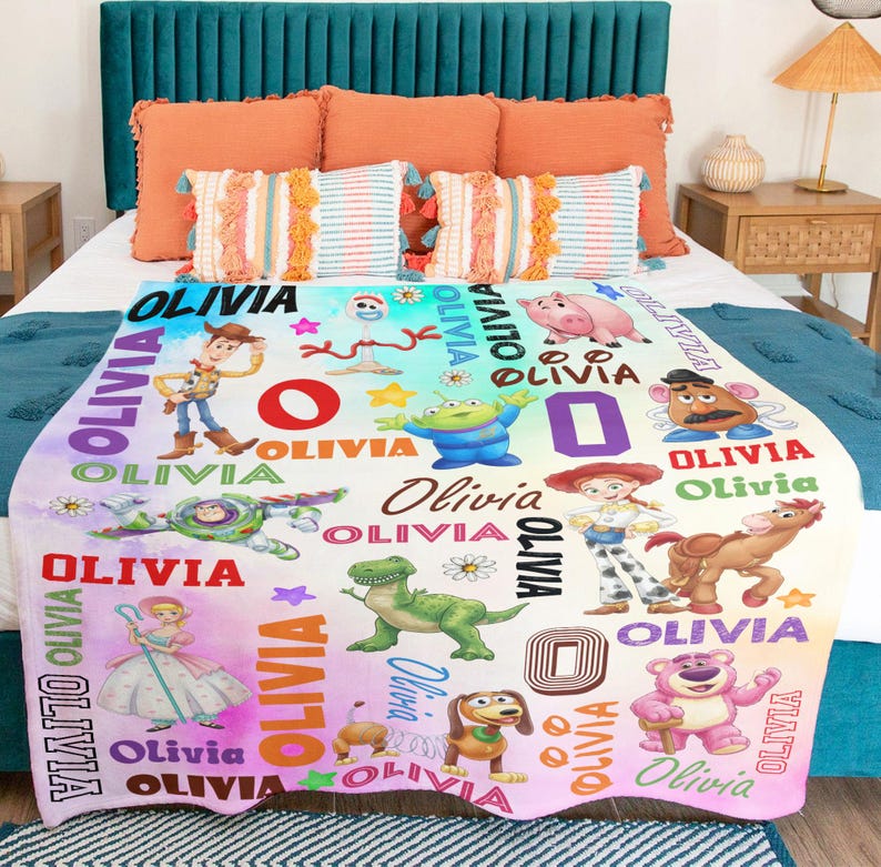 May include: A white fleece blanket featuring a colorful print of various animated characters including a cowboy, space ranger, cowgirl, dinosaur, pig, and bear. The name Olivia is printed repeatedly in multiple fonts and colors across the fabric.