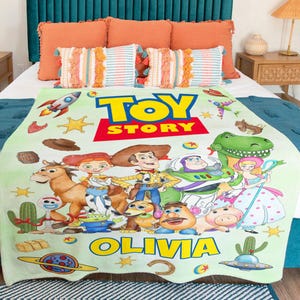 May include: A light green fleece blanket featuring the Toy Story logo, the name Olivia, and various characters including Woody, Buzz Lightyear, Jessie, Bullseye, Rex, and Mr. Potato Head, decorated with colorful space and western themed icons.