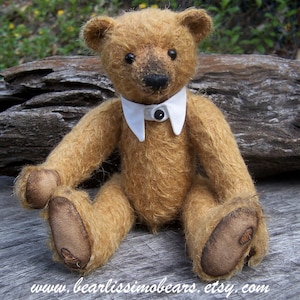 May include: A brown teddy bear wearing a white collared shirt with a black button. The bear is sitting on a wooden surface.