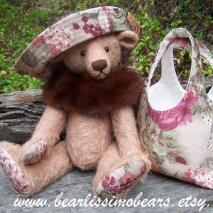 May include: A handmade teddy bear with a brown fur collar and a matching hat, sitting next to a tote bag. The bear and bag feature a floral pattern with pink and green accents. The bear's paws also have the floral pattern.