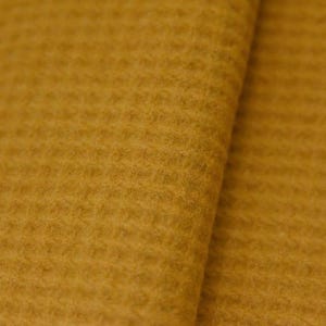 Puede incluir: Primer plano de una tela texturizada de color amarillo mostaza. El material tiene un patrón acanalado, con líneas horizontales visibles. La tela parece suave y posiblemente de lana o un material similar. El color es un tono cálido y terroso.