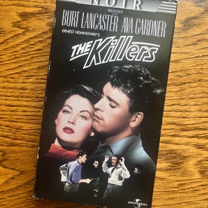 May include: A VHS tape cover for the film "The Killers", a 1946 film noir starring Burt Lancaster and Ava Gardner. The cover features a black and white image of Lancaster and Gardner in a close-up shot. The title "The Killers" is in large white letters with a red outline. The text "Ernest Hemingway's" is in smaller white letters below the title. The Universal logo is in the bottom right corner.