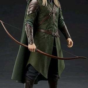 Puede incluir: Figura detallada de un personaje de una película de fantasía, vestido con una túnica verde, capa y botas. La figura sostiene un arco y una flecha, con un carcaj de flechas en la espalda. El personaje tiene el pelo largo y rubio y está de pie sobre una base de piedra.