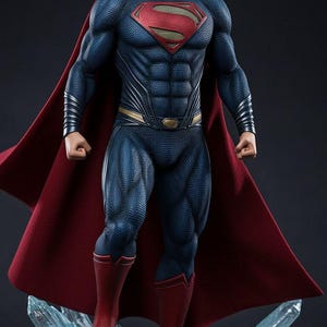Puede incluir: Estatua detallada de Superman. La figura está en una pose dinámica, vistiendo un traje azul con un emblema rojo y dorado, una capa roja y botas rojas. La estatua está montada sobre una base rocosa con formaciones cristalinas.