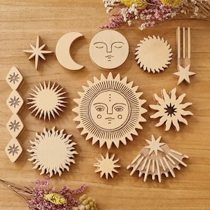 Puede incluir: Una colección de recortes de madera de color claro con formas celestiales, que incluyen un sol grande con cara, una luna creciente con cara, varios rayos de sol, una estrella y una tira vertical en forma de diamante con cuatro pequeñas estrellas.