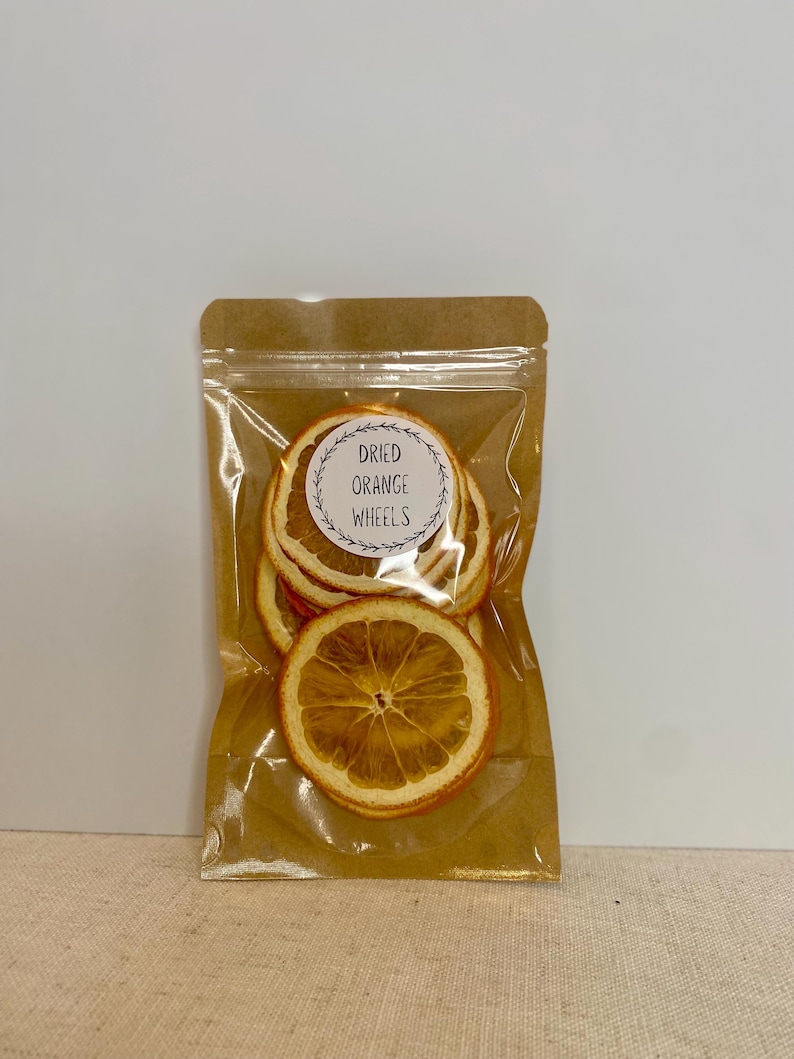 May include: A clear plastic bag filled with dried orange wheels. The bag is sealed and attached to a brown paper backing. The label on the bag reads "Dried Orange Wheels" in a circular design.