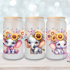 May include: Three white tumblers with lids and straws. Each tumbler features a different cartoon elephant wearing a flower crown. The elephants are gray with pink ears and are holding a pink bow.