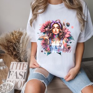 May include: White t-shirt with a graphic print of a woman with tattoos and flowers. The woman is wearing a denim overall and has a pink bandana in her hair. The text "Fearless" is printed on the shirt.