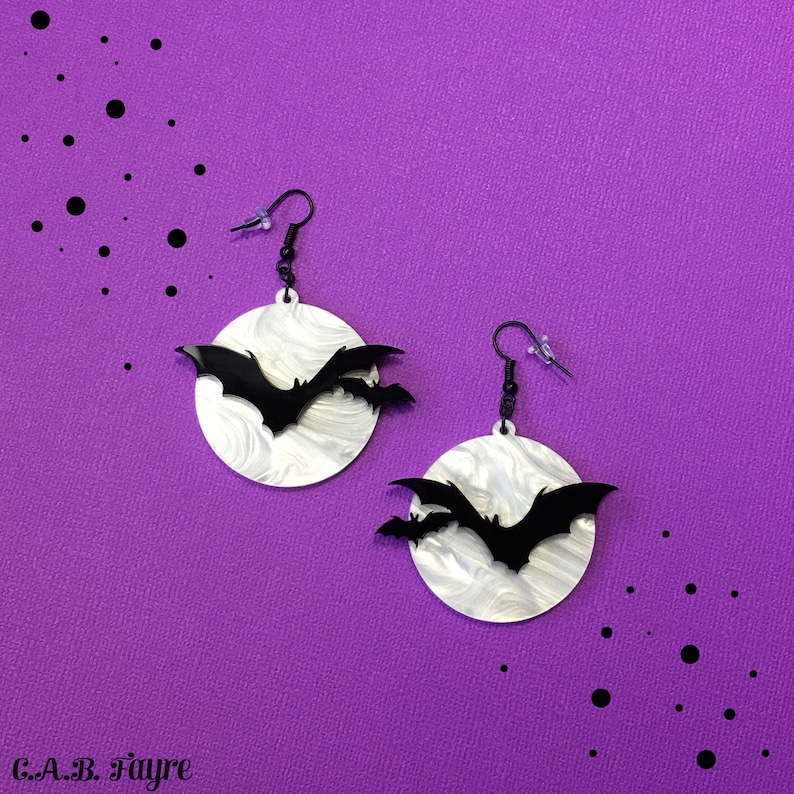 White pearl marble moon earrings with black bats, spooky Halloween earrings displayed on purple background.