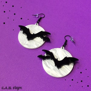 Ghostly bat earrings with shimmering white pearl moon and black acrylic bats, gothic Halloween jewelry flat lay.