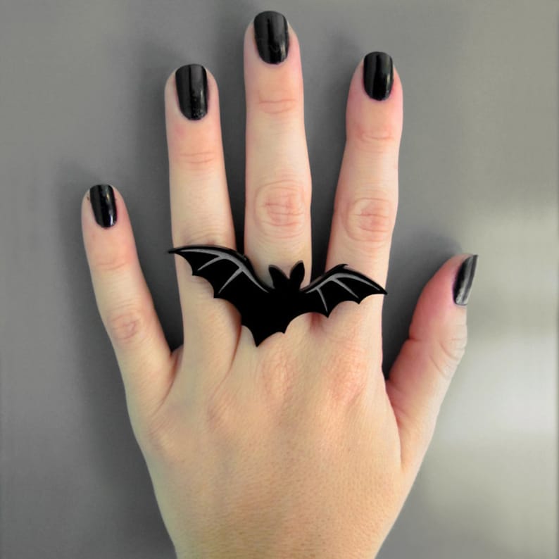 Hand wearing large Vampire Bat Ring spanning across three fingers – black acrylic statement ring with engraved wing details.