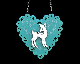 May include: A turquoise blue heart-shaped pendant necklace with a white silhouette of a deer inside. The heart has a scalloped edge and a delicate floral pattern.