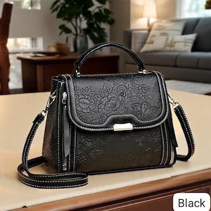 May include: Black handbag with a floral embossed design. The bag features a top handle, a detachable shoulder strap, and a flap closure with a silver-tone clasp. White stitching accents the edges and zippers. The word "Black" is in the bottom right corner.