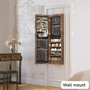 May include: A wall-mounted, wooden jewelry armoire with an open door, revealing various necklaces, earrings, and other jewelry. The armoire is brown with a black interior and is mounted on a white door. The text "Wall mount" is visible at the bottom.
