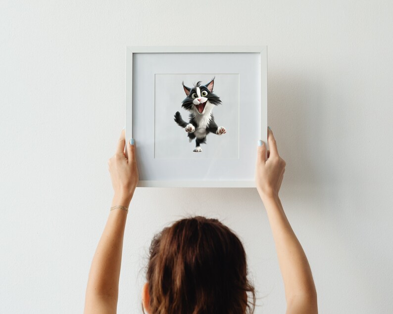 May include: A person hangs a white framed picture on a white wall. The picture features a cartoon black and white cat with a surprised expression.