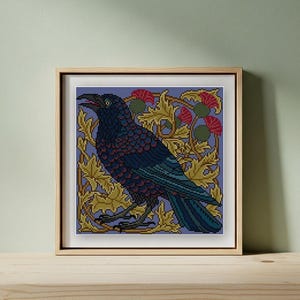 May include: Framed cross-stitch art featuring a detailed raven with open beak, in shades of blue and black. The bird is set against a background of stylized gold leaves and red thistle flowers, all on a purple backdrop. The artwork is in a wooden frame.