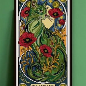 May include: Art print in a black frame, depicting a green cat amidst red poppies and decorative foliage. The design has a vintage feel, with the word "TAURUS" at the base. The colour scheme includes green, red, blue, and gold, reminiscent of Art Nouveau.