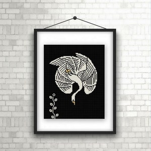 May include: A black and white cross-stitch pattern of a stylized crane with its wings spread wide. The crane is white with a yellow beak and is set against a black background. A small, stylized plant is in the lower left corner.