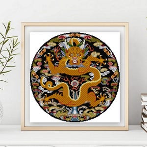 Könnte beinhalten: Gerahmte Kreuzstichkunst mit einem goldenen Drachendesign auf schwarzem Hintergrund. Der Drache ist von bunten Wolken und dekorativen Elementen umgeben. Das Kunstwerk wird in einem quadratischen, hellfarbigen Holzrahmen präsentiert.