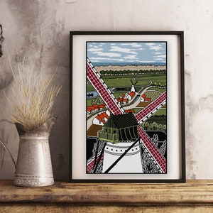 May include: A framed illustration of a windmill with red blades against a blue sky. The windmill is surrounded by a small village with green fields and trees.