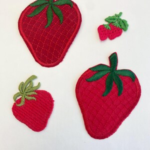 May include: Three embroidered strawberry patches in varying sizes. Each patch features a bright red fruit body with a textured, cross-hatched pattern and a green leafy stem at the top. The patches are arranged in a cluster against a plain background.