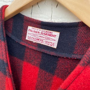 May include: A set of three ceramic mugs with a speckled, cream-colored glaze. Each mug features a different hand-painted design: a blue and green leaf, a yellow and orange flower, and a red and pink berry. The mugs have a simple, rounded shape.