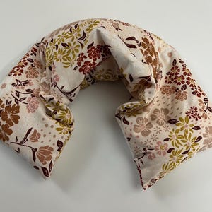 Peut inclure: Un coussin de cou en forme de croissant avec une base en tissu crème ornée d'un motif floral répétitif dans des tons orange rouille, vert olive doux et rose pâle. Le coussin présente une forme incurvée conçue pour le cou et les épaules.