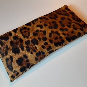 May include: A brown and black leopard print eye pillow. The pillow is rectangular and has a soft, plush texture.