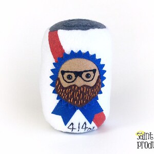 Puede incluir: Un juguete de peluche con forma de lata de cerveza con una cinta azul y una cara de dibujos animados con gafas y barba. La cinta tiene el texto "414" en ella.