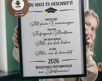May include: A framed graduation print featuring the German text DU HAST ES GESCHAFFT! with a graduation cap icon, followed by inspirational phrases about memories, adventures, loved ones, and inner strength, ending with 2026 and Staatsexamen.