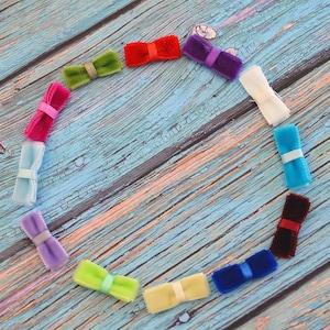 Könnte beinhalten: Eine Anordnung aus farbigen Samtschleifen, die kreisförmig auf einer verwitterten, blauen Holzoberfläche angeordnet sind. Die Schleifen sind in verschiedenen Farben wie Rot, Grün, Lila und Blau gehalten und mit passenden oder kontrastierenden Bändern gebunden. Thema: Basteln oder Accessoires.