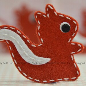 May include: A handcrafted felt squirrel in a bright red hue, with a white belly and tail, and a black eye. The squirrel is stitched with white thread, giving it a charming, handmade look. Ideal for children.