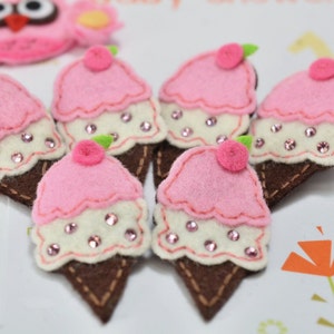 May include: A collection of handmade felt ice cream cone decorations. Each cone features a pink ice cream scoop with a cherry on top, embellished with rhinestones. A pink owl decoration is also visible.