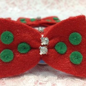 May include: Red felt bow with green polka dots and a rhinestone center. Several bows are visible, suggesting a set or collection. The bows are likely for crafts, accessories, or decorations.